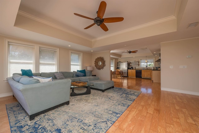 living room with a raised ceiling, wood-type flooring, ornamental molding, and ceiling fan