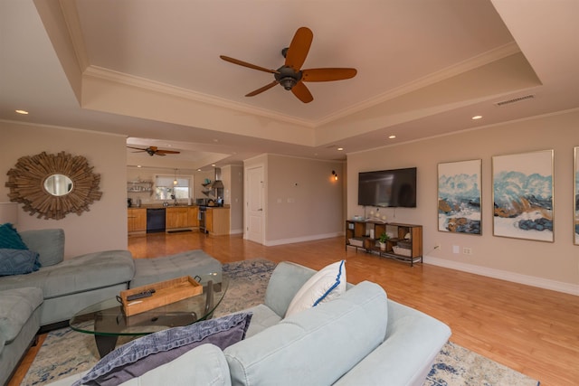 living room featuring crown molding, light hardwood / wood-style floors, and a raised ceiling