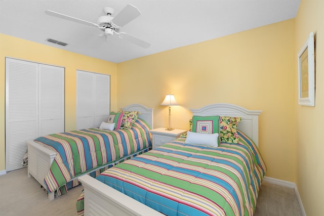 bedroom featuring multiple closets, visible vents, a ceiling fan, light carpet, and baseboards