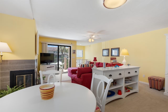 carpeted dining space with ceiling fan, baseboards, and a tiled fireplace