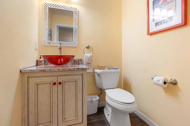 half bathroom featuring wood finish floors, vanity, toilet, and baseboards