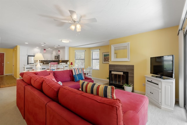 living area featuring baseboards, light colored carpet, a ceiling fan, and a glass covered fireplace