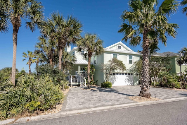 coastal home featuring decorative driveway, covered porch, an attached garage, and central AC unit