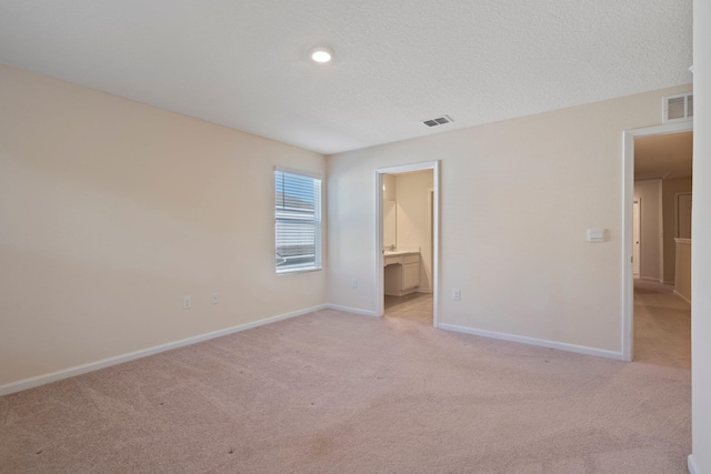 unfurnished bedroom with connected bathroom, light carpet, and a textured ceiling