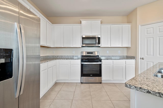 kitchen with white cabinets, appliances with stainless steel finishes, light tile patterned floors, and light stone counters