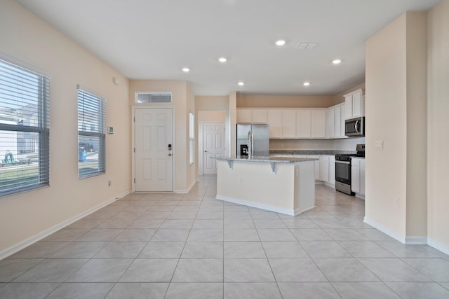 kitchen with white cabinets, appliances with stainless steel finishes, an island with sink, a kitchen breakfast bar, and stone counters