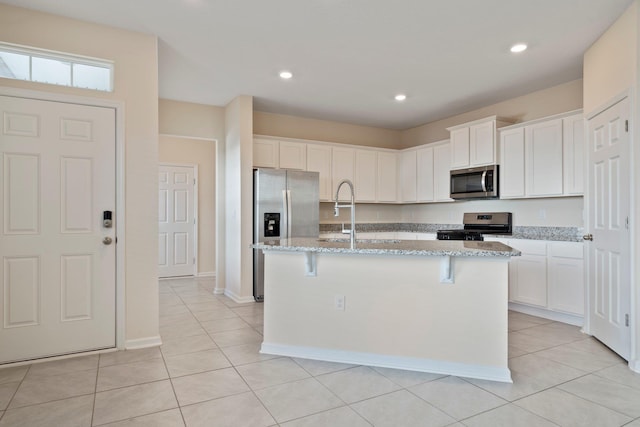 kitchen with light stone countertops, sink, appliances with stainless steel finishes, and an island with sink