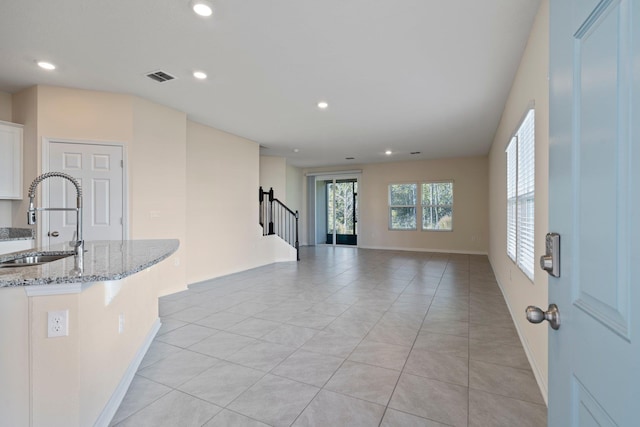 interior space with sink, light tile patterned floors, light stone countertops, a breakfast bar area, and white cabinets