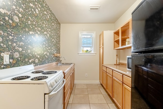 kitchen with electric range, sink, light tile patterned flooring, and light brown cabinets