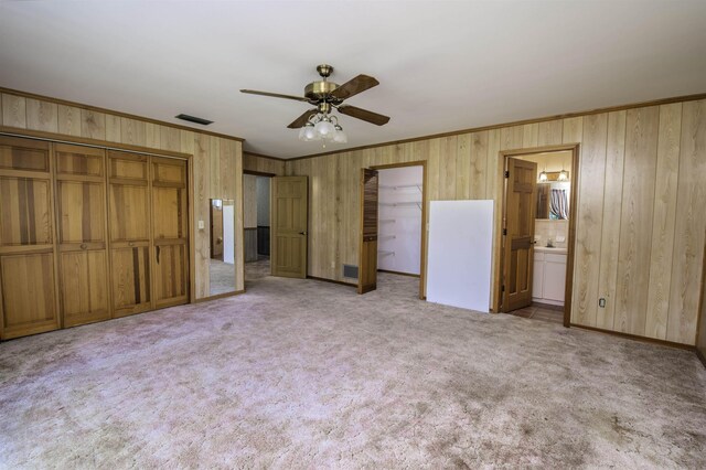 unfurnished bedroom featuring ceiling fan, two closets, light colored carpet, and ensuite bath