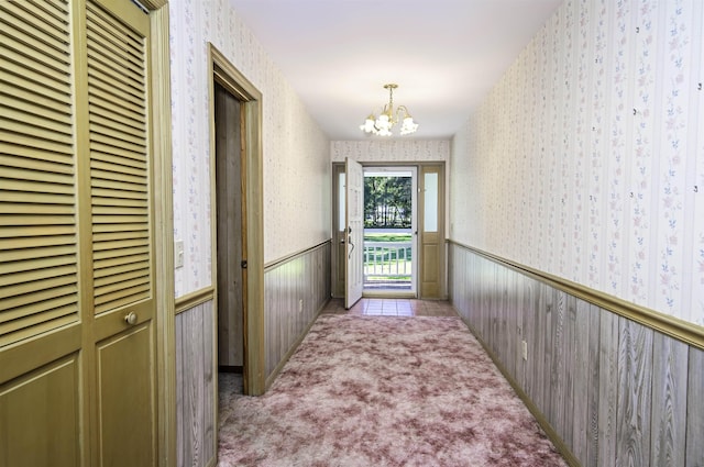 entryway featuring light colored carpet, an inviting chandelier, and wooden walls