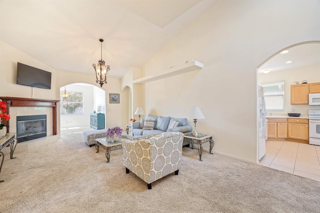 living area with arched walkways, light tile patterned floors, light colored carpet, a tiled fireplace, and vaulted ceiling