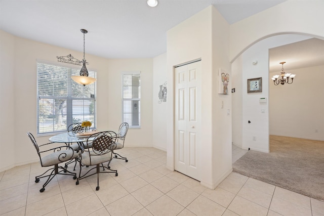 dining area with arched walkways, a notable chandelier, light tile patterned floors, light colored carpet, and baseboards