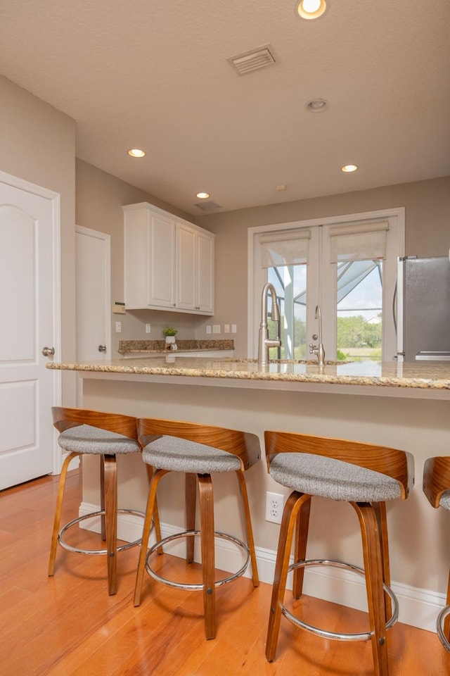 517 Weeping Willow Ln, Saint Augustine, FL 32080 - kitchen featuring freestanding refrigerator, white cabinets, recessed lighting, light stone counters, and a kitchen bar