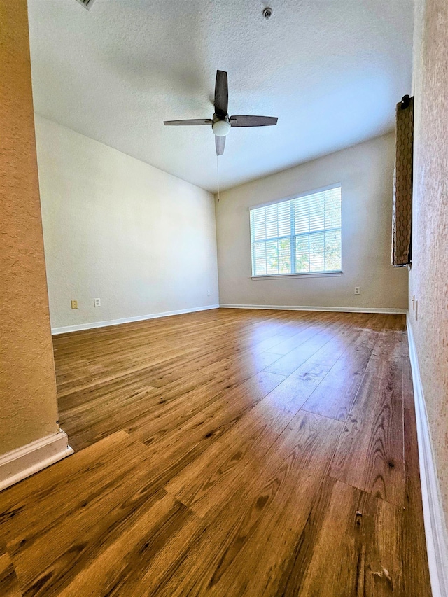 spare room with ceiling fan, a textured ceiling, baseboards, and hardwood / wood-style flooring