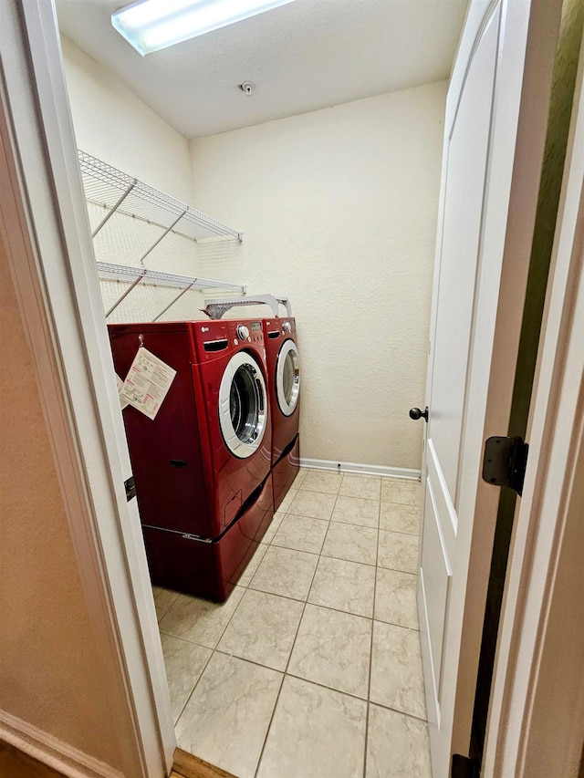 clothes washing area with laundry area, washer and clothes dryer, baseboards, and light tile patterned floors