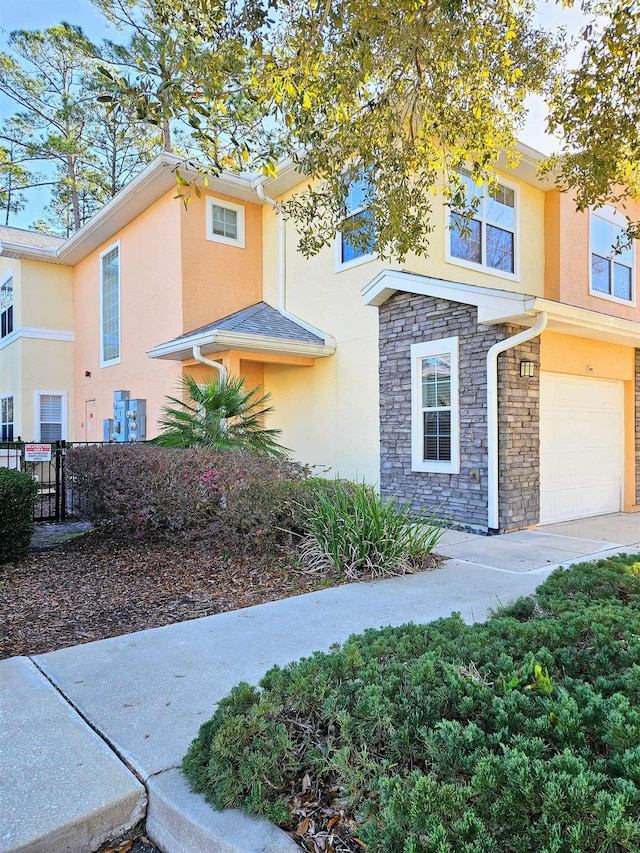 view of front facade featuring stone siding, an attached garage, fence, and stucco siding