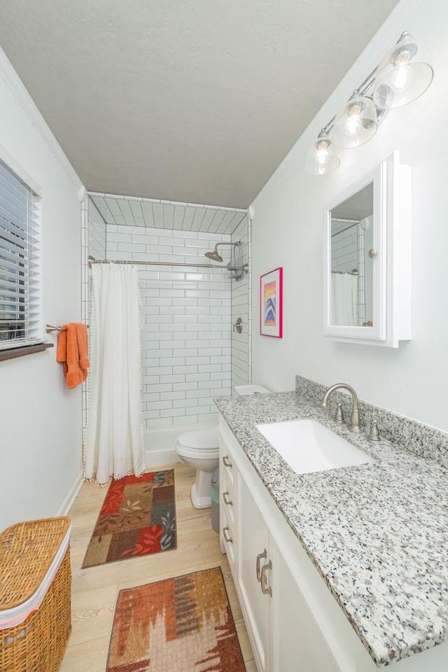 bathroom with toilet, tiled shower, wood finished floors, and vanity