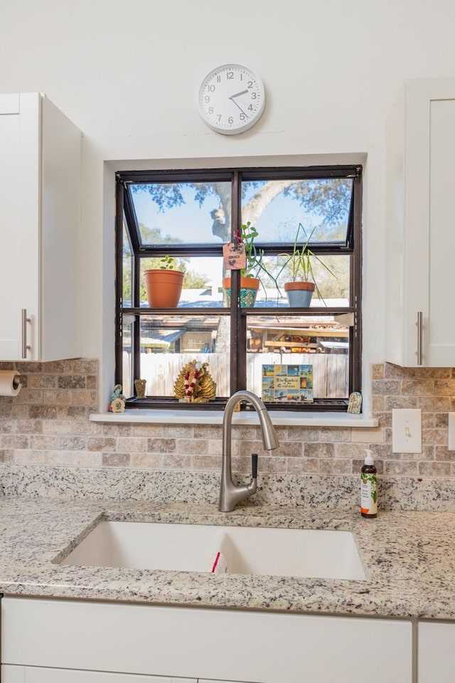 interior details with light stone countertops, tasteful backsplash, white cabinetry, and a sink