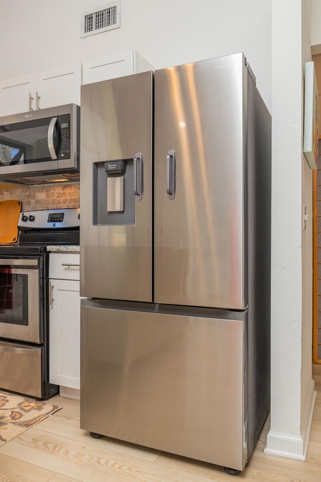 kitchen with light wood finished floors, appliances with stainless steel finishes, visible vents, and white cabinetry