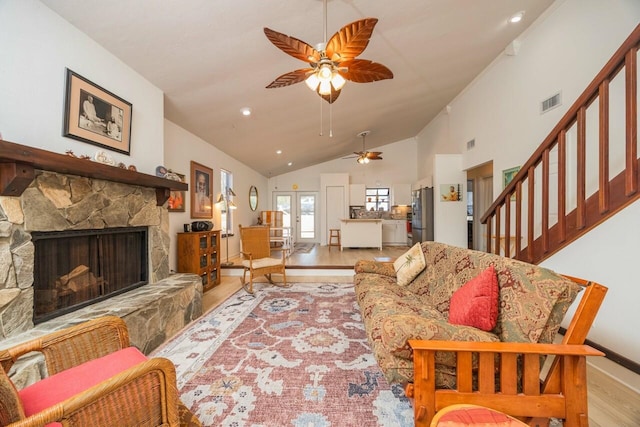 living room featuring high vaulted ceiling, a stone fireplace, wood finished floors, visible vents, and stairway