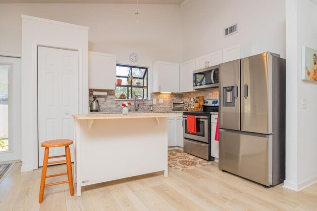 kitchen with white cabinets, visible vents, stainless steel appliances, and a breakfast bar area