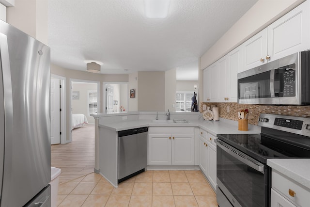 kitchen featuring a peninsula, light countertops, white cabinetry, a sink, and appliances with stainless steel finishes