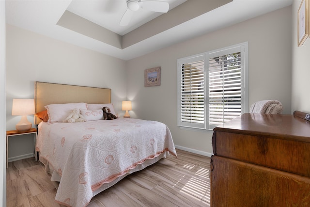 bedroom featuring a ceiling fan, baseboards, wood finished floors, and a raised ceiling