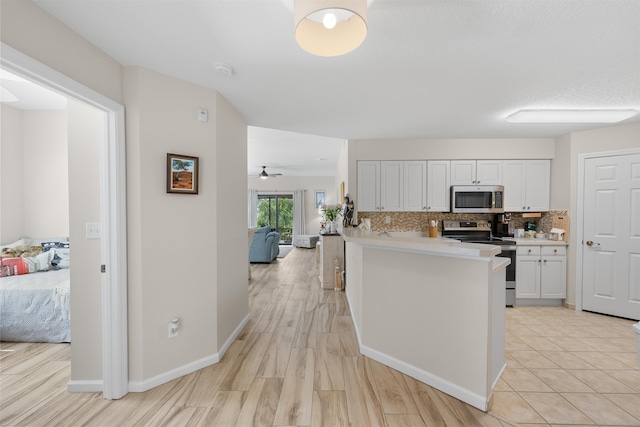 kitchen featuring appliances with stainless steel finishes, light countertops, white cabinetry, a peninsula, and tasteful backsplash