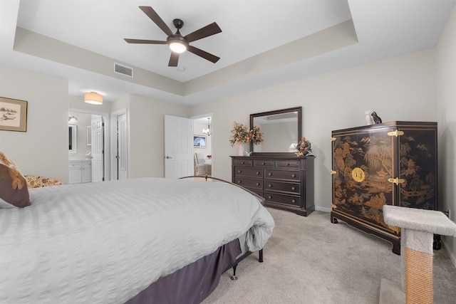 bedroom featuring light carpet, a raised ceiling, ensuite bath, a ceiling fan, and visible vents