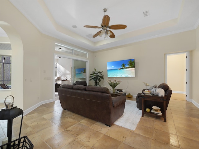 living room featuring arched walkways, a raised ceiling, visible vents, and baseboards