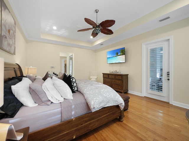 bedroom with visible vents, baseboards, a raised ceiling, a ceiling fan, and light wood-style floors