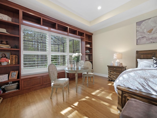 bedroom with light wood-style floors, recessed lighting, a tray ceiling, and baseboards