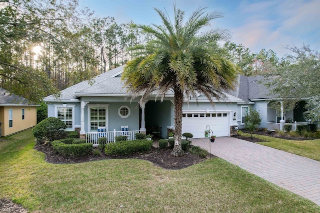 ranch-style home with an attached garage, a front lawn, a porch, and decorative driveway