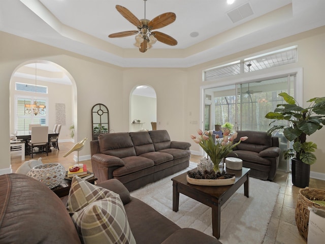 living room with visible vents, a tray ceiling, arched walkways, and ceiling fan with notable chandelier