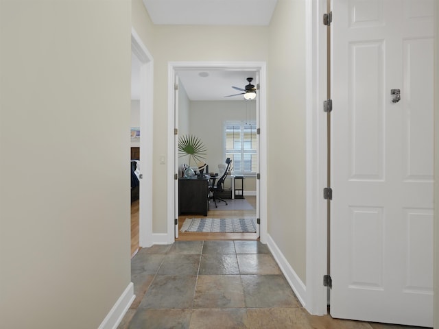 hall featuring baseboards and stone tile flooring