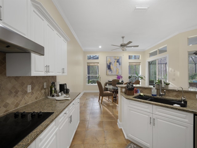 kitchen featuring a sink, white cabinetry, ornamental molding, dark stone counters, and black stovetop