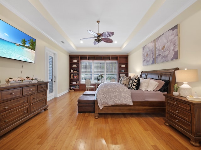 bedroom featuring ceiling fan, visible vents, baseboards, light wood-type flooring, and a tray ceiling