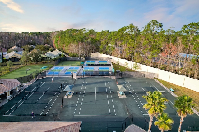 view of tennis court with a wooded view and fence