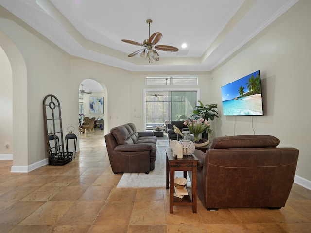 living room with baseboards, arched walkways, ceiling fan, stone finish flooring, and a tray ceiling