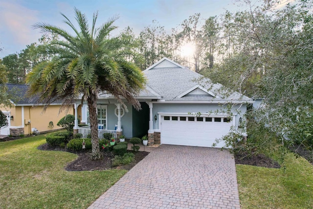 view of front of property with a porch, a garage, decorative driveway, a lawn, and stucco siding