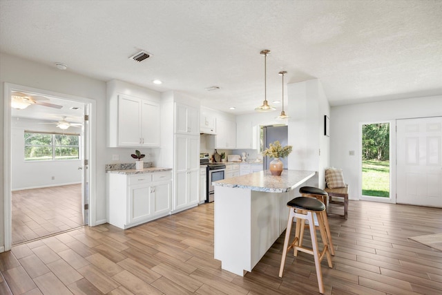 kitchen with stainless steel range with electric stovetop, a healthy amount of sunlight, white cabinets, and light hardwood / wood-style floors