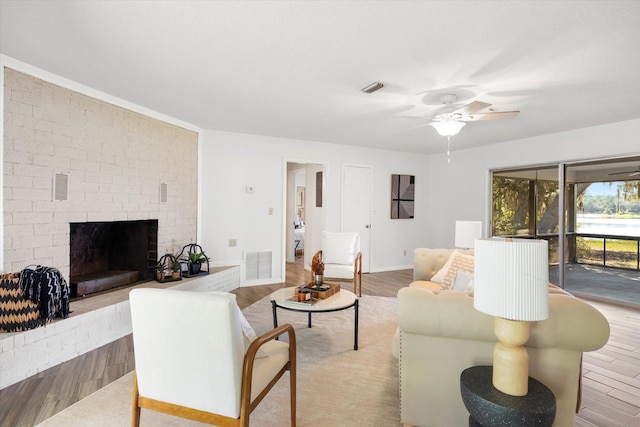 living room featuring a brick fireplace, light hardwood / wood-style flooring, and ceiling fan