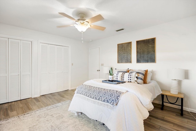 bedroom with wood-type flooring, ceiling fan, and multiple closets