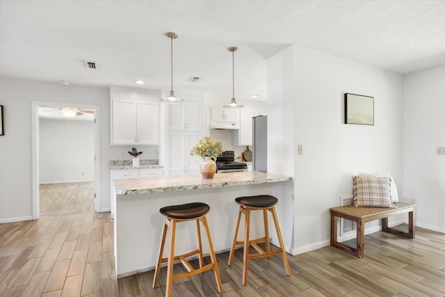 kitchen with light wood-type flooring, black range with electric cooktop, white cabinetry, and hanging light fixtures