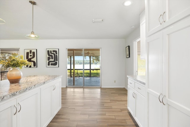 kitchen with white cabinetry, light stone counters, decorative light fixtures, and light wood-type flooring