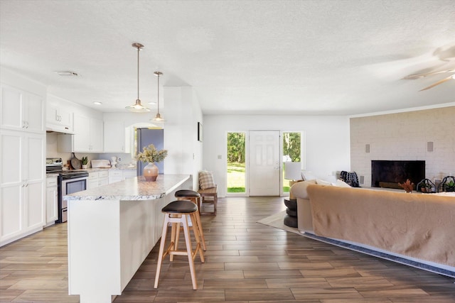 kitchen with white cabinetry, stainless steel electric range oven, a kitchen breakfast bar, pendant lighting, and hardwood / wood-style flooring