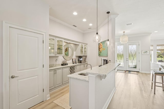 104 Fiddler Crab Ln, Saint Augustine, FL 32080 - kitchen featuring crown molding, glass insert cabinets, french doors, light wood-style floors, and light stone counters