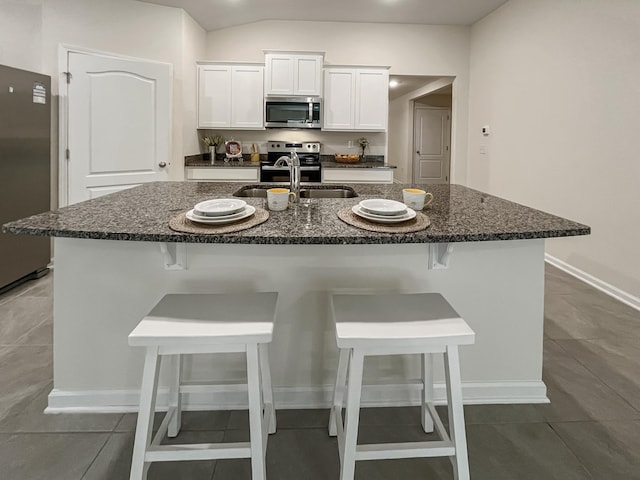 kitchen with a kitchen breakfast bar, stainless steel appliances, sink, a center island with sink, and white cabinetry