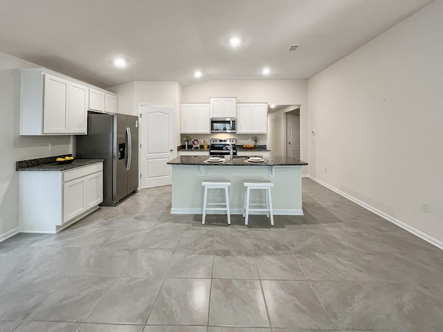 kitchen with a kitchen island with sink, dark stone counters, white cabinets, appliances with stainless steel finishes, and a kitchen bar